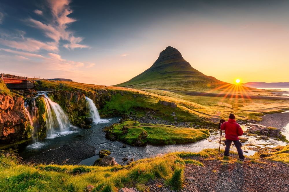 A hiker enjoys sunrise views over lands and waterfalls in their puffer jacket and beanie because they knew what to wear to Iceland in the fall.
