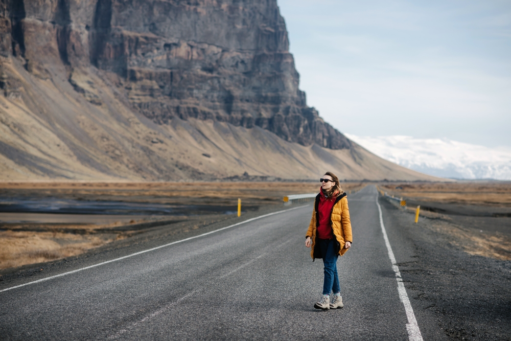 A woman walks down a road by a cliff in Iceland in her jeans, hiking boots, hoodie and parka: she knew what to wear to Iceland in the fall.