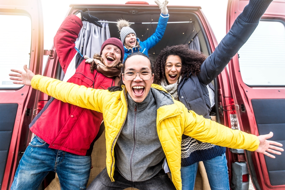 A group of friends pose outside a car in Iceland, all wearing down jackets and then parkas over them, their warms spread wide and huge smiles on their faces since they knew what to wear in Iceland in November.