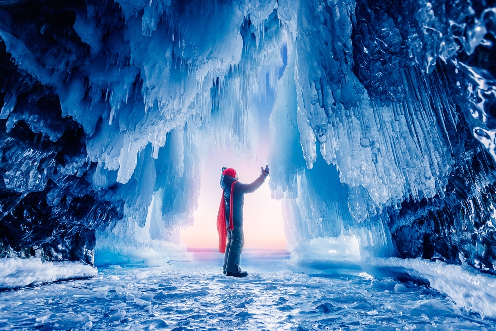A tourist knows exactly what to wear in Iceland in November when exploring ice caves in their red wool scarf, matching wool red beanie, parka, gloves, pants and boots.