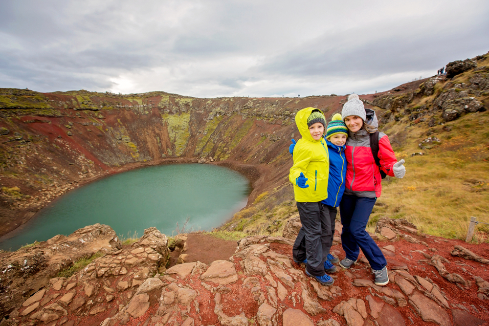 Three kid stand in front of a landmark in Iceland, all in waterproof pants, books, hats and jackets, well prepared with what to wear in Iceland for kids.
