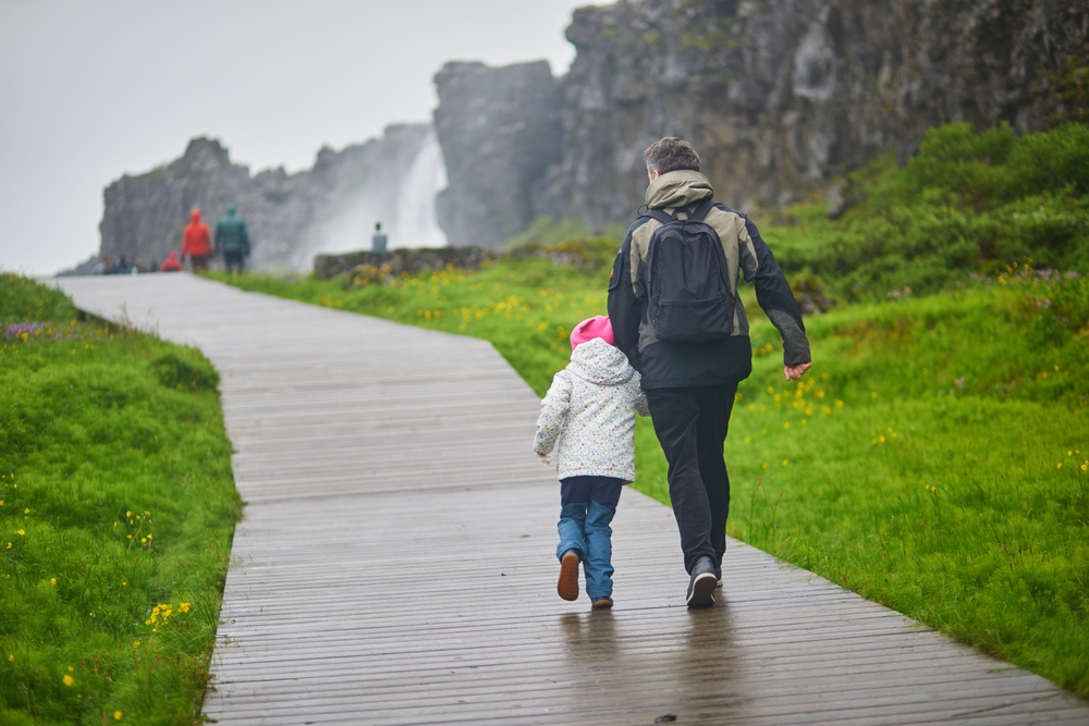 A father and his child walks down a path in Iceland in down jackets, on a walk way, in the rain, prepared since they knew what to wear in Iceland for kids.
