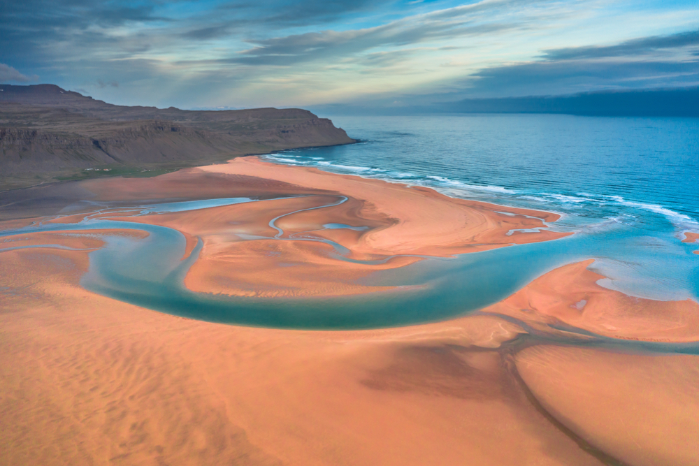 The beautiful red sand beaches of Rauosaundur with the turquoise water and sky in the background