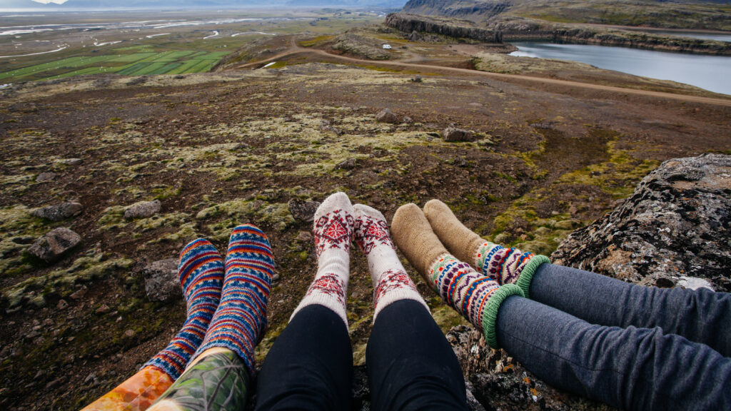Three girls point their wool-clad toes together against the terrain of Iceland, their hiking pants tucked into the warmth of their socks. 