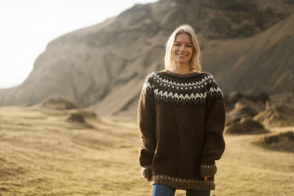 A classic woman in a traditional Icelandic sweater smiles against the rugged terrain of Iceland during golden hour. 