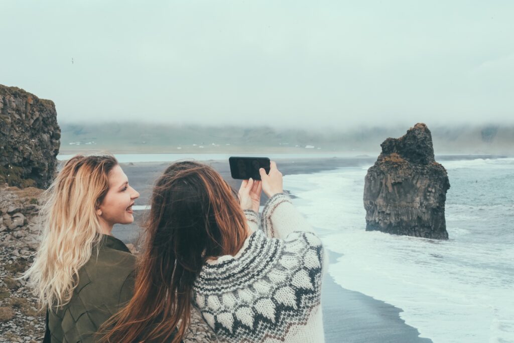 Two friends pose for a selfie on a foggy coastal day, their green jackets and knit wool sweaters keeping them warm. 