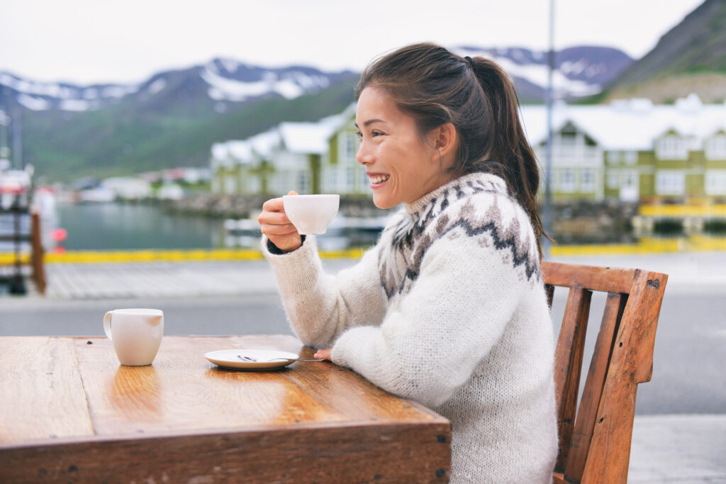 A woman relaxes at a cafe, drinking coffee in a wool sweater, hair up, knowing what to wear in Reykjavik for a casual day. 