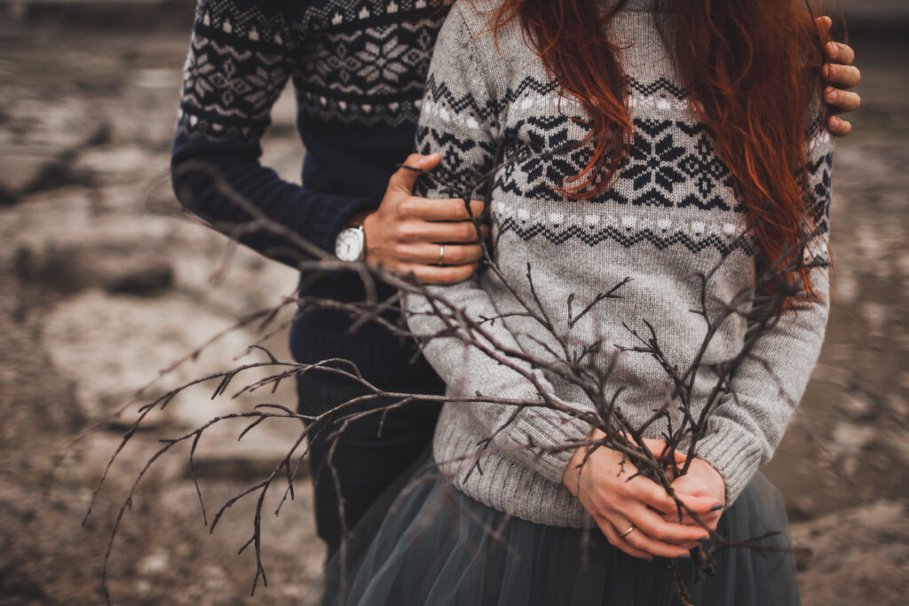 A man holds a woman's arms as she poses against icy terrain in a skirt and classic Icelandic sweater, knowing what to wear in Reykjavik.